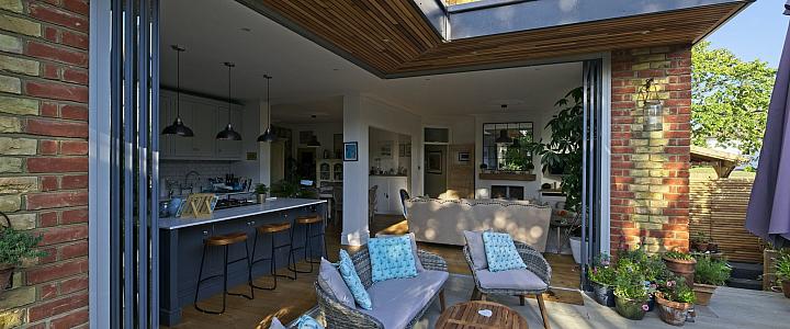 Frameless corner doors opening without a corner post on a brick home extension, revealing the garden beyond