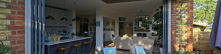 Frameless corner doors opening without a corner post on a brick home extension, revealing the garden beyond