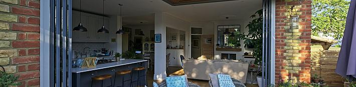Frameless corner doors opening without a corner post on a brick home extension, revealing the garden beyond