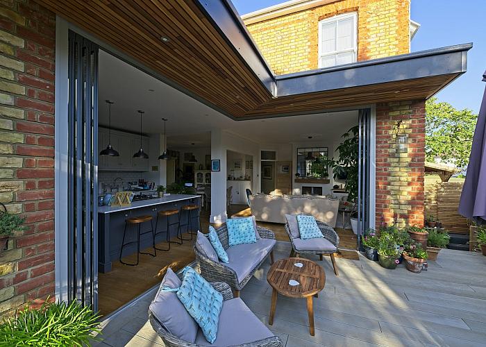 Frameless corner doors opening without a corner post on a brick home extension, revealing the garden beyond